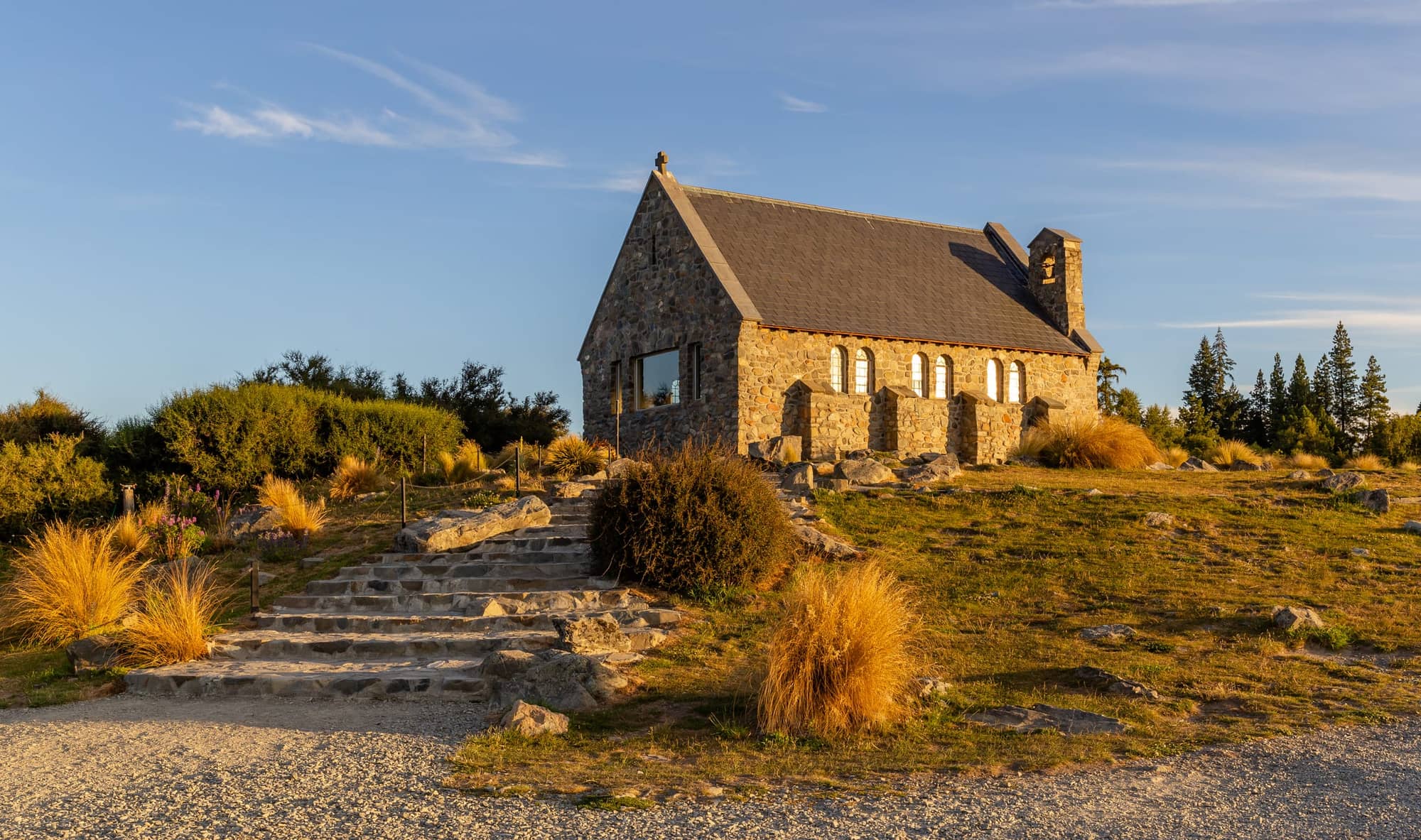 Stone chapel on a tussock-covered hillside lit by golden evening light